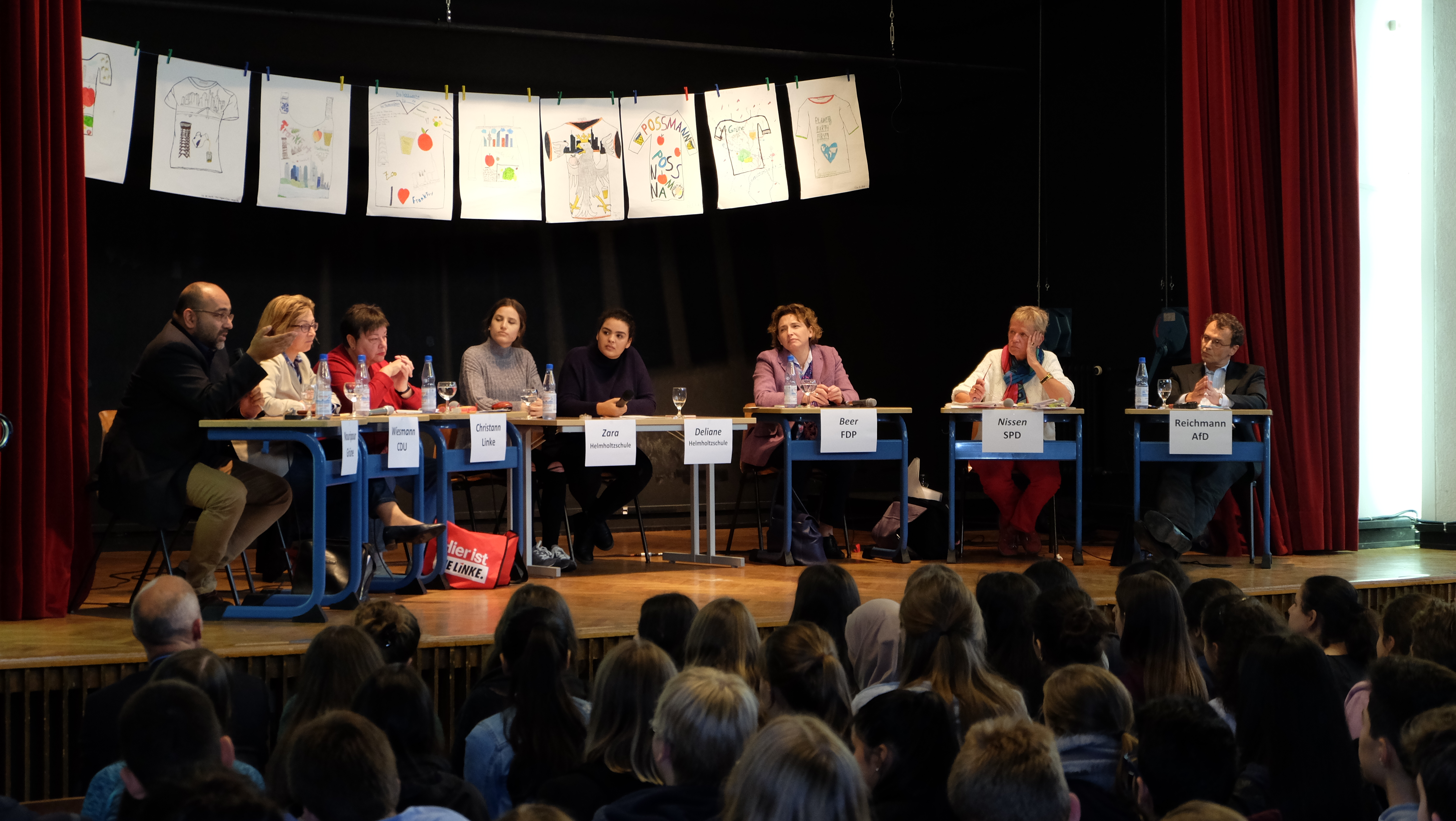 sechs Frankfurter Direktkandidatinnen und Direktkandidaten in einer prall gefüllten Aula der Helmholtzschule